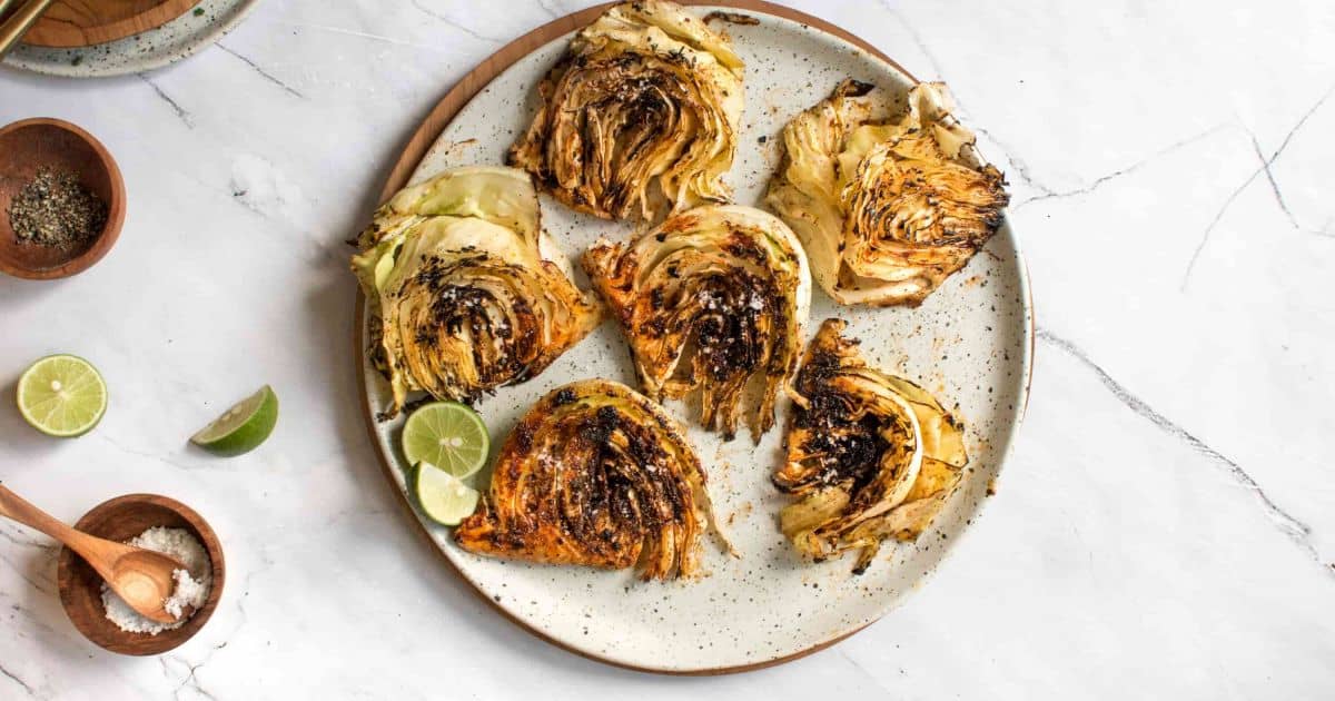Overhead shot of grilled cabbage on a white plate with lime, salt, and seasonings.