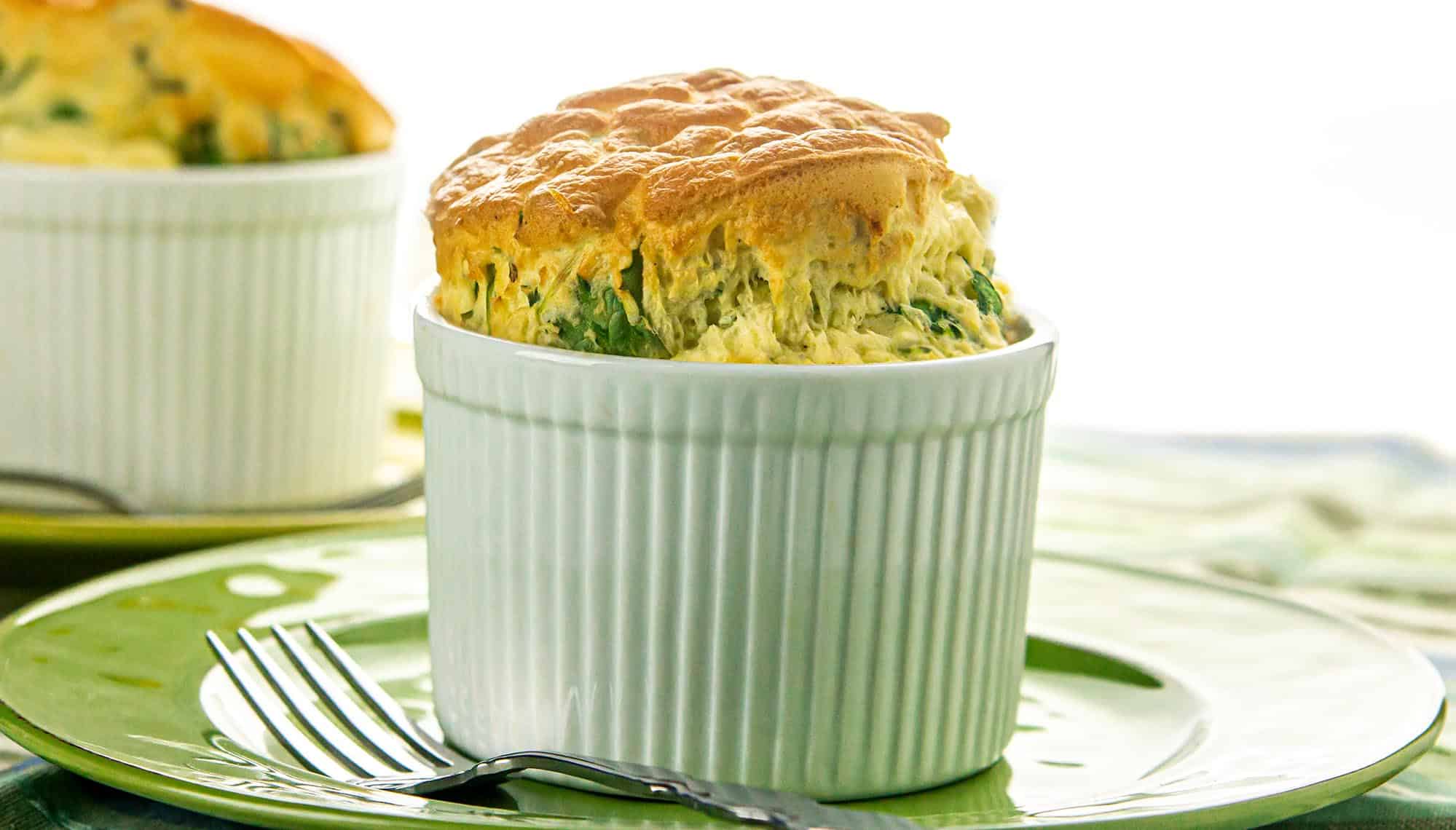 A straight view of air-fried arugula and cheddar egg soufflés in a ramekin above a green plate.