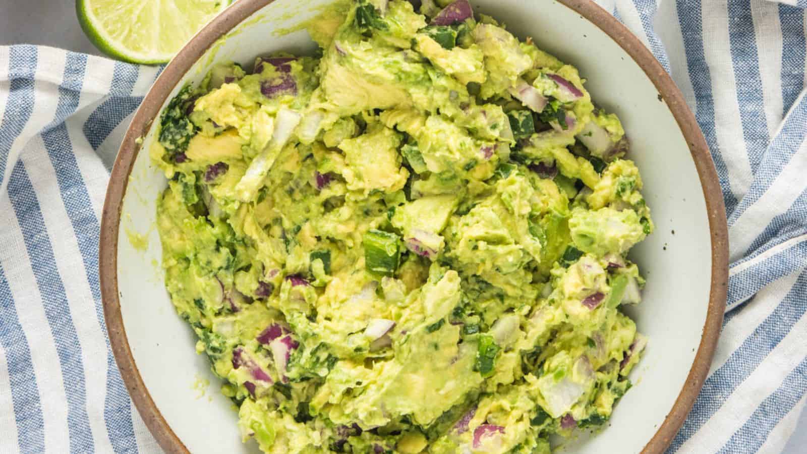 Close up of chunky guacamole with a blue and white striped napkin under. 