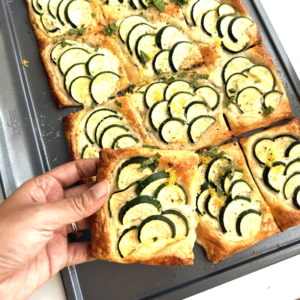 Slice of zucchini puff pastry tart with lemon ricotta lifted from the baking tray.