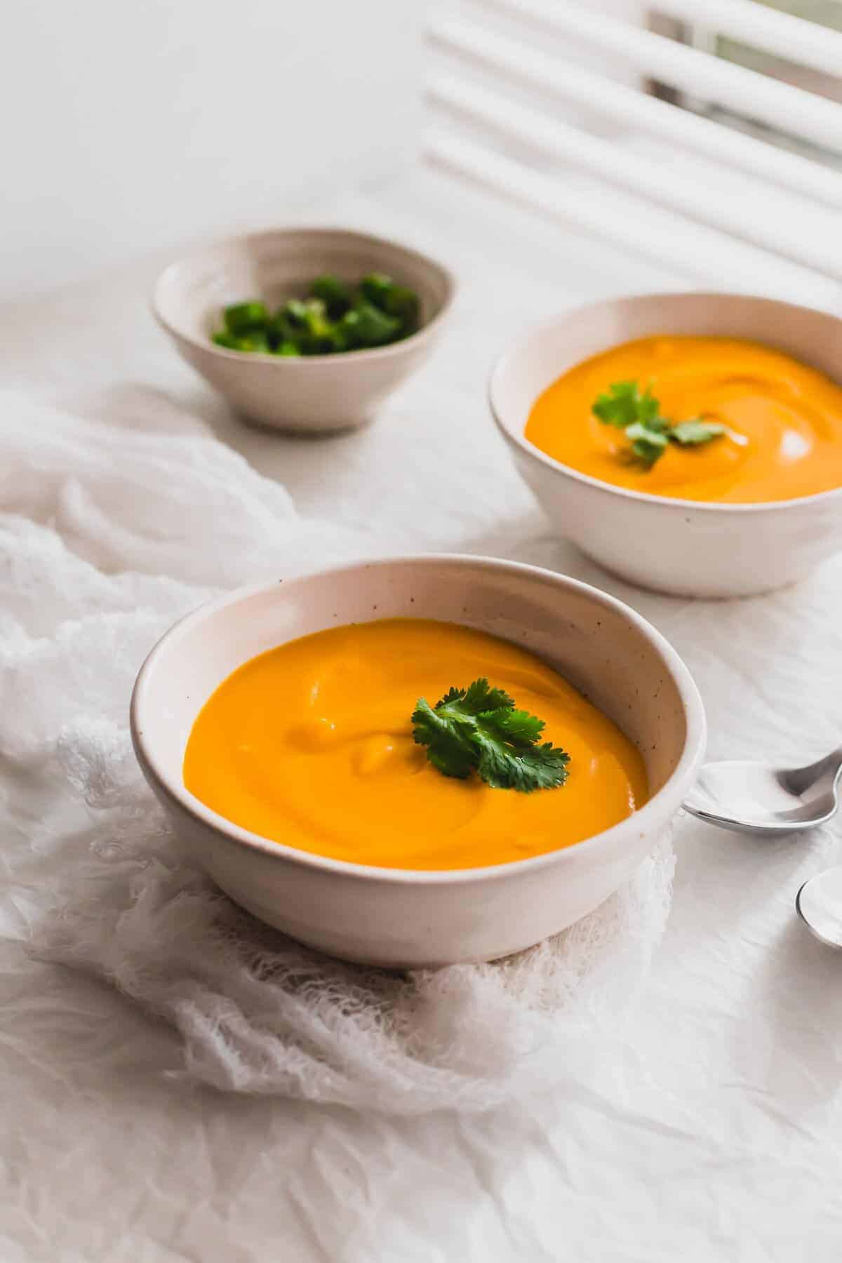 Close up of kabocha squash soup in white bowls, with a white napkin.