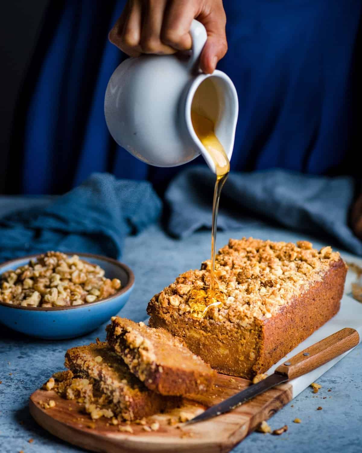 Hand shown to be pouring drizzle over a kabocha squash banana bread with blue backdrops.