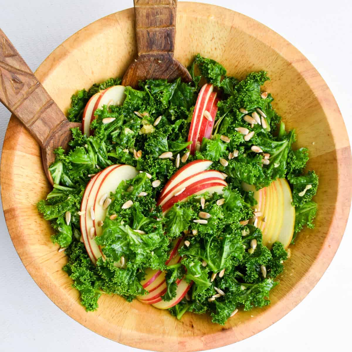 Overhead view of a wooden bowl with kale salad topped with sunflower seeds and sliced apples.