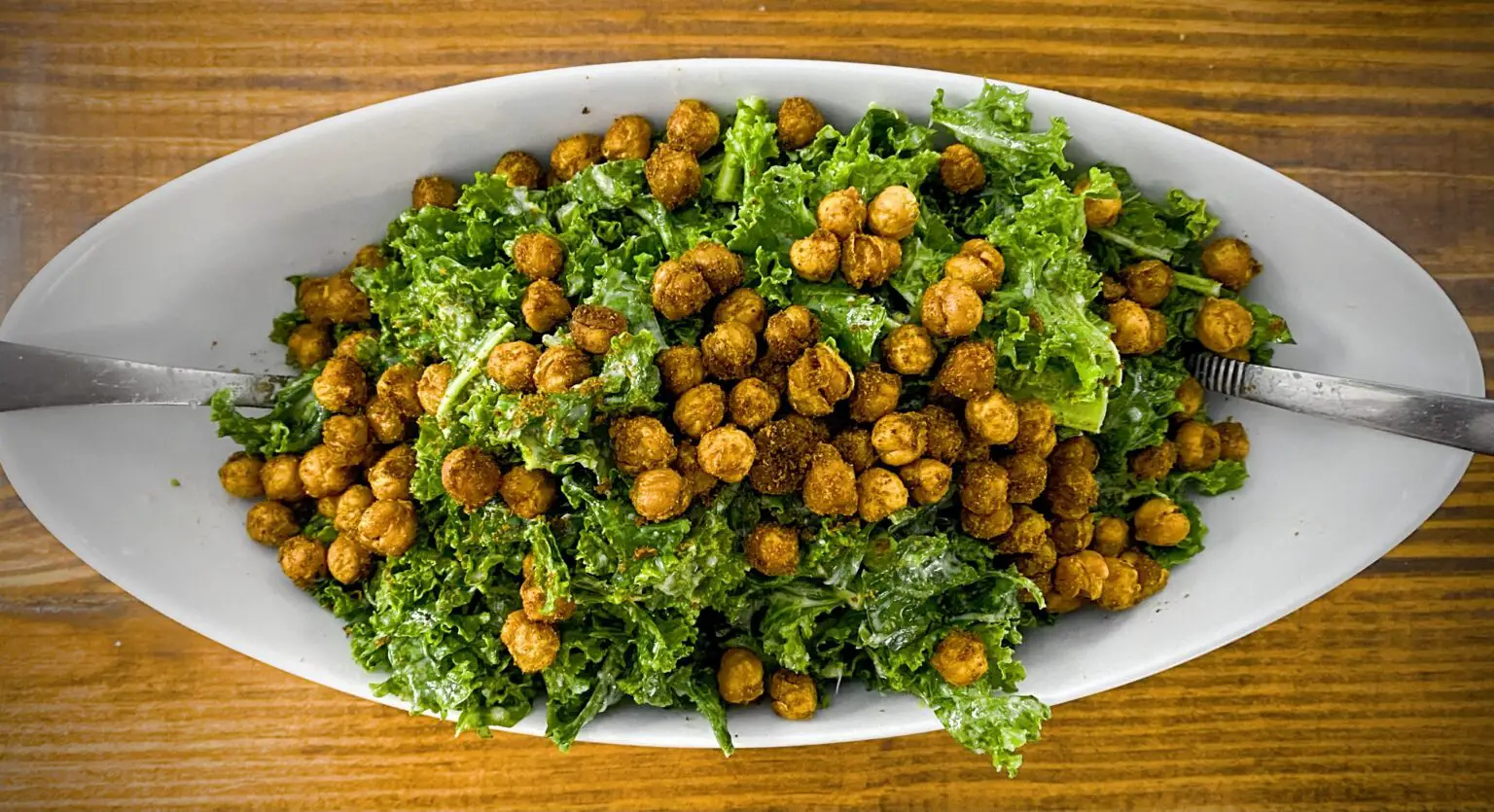 Overhead view of an oval-shaped plate filled with kale salad and spicy chickpeas.