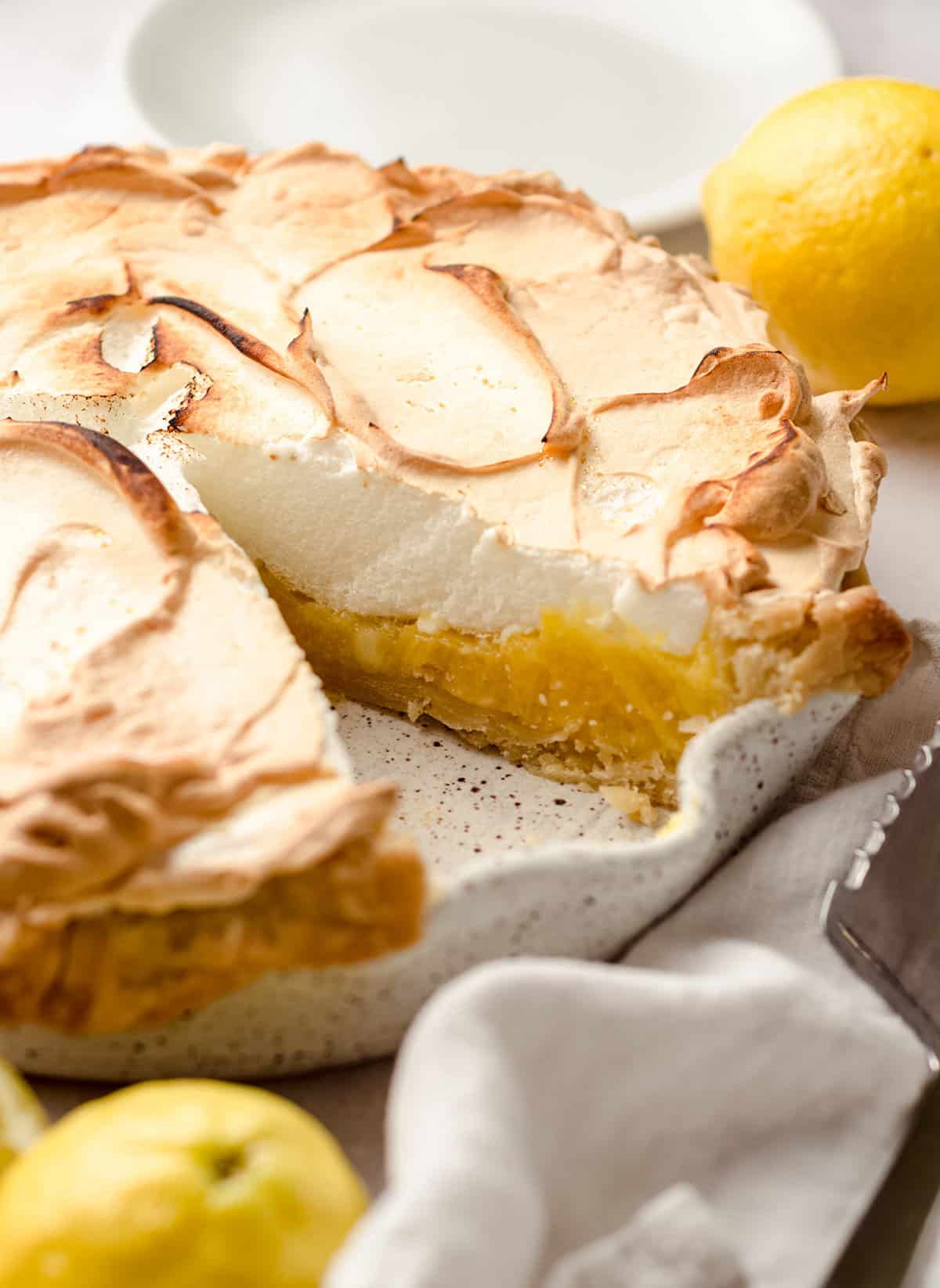 Close up of lemon meringue pie with a slice cut out, with white napkin in foreground.
