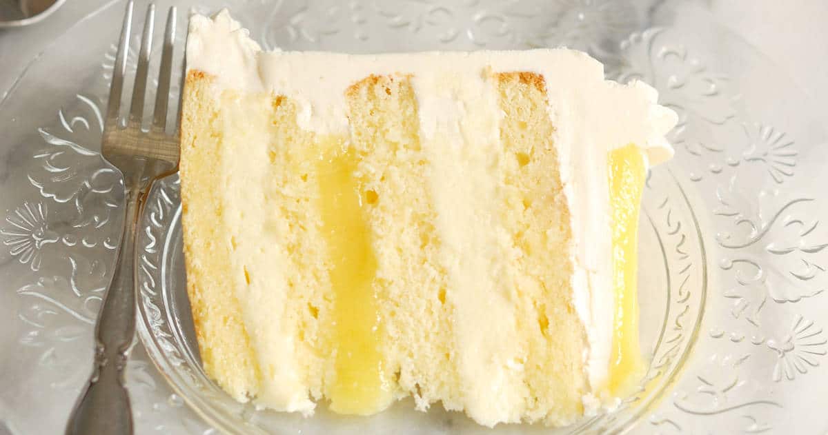A close-up view of sliced luscious lemon mousse cake with a fork placed on a glass plate.