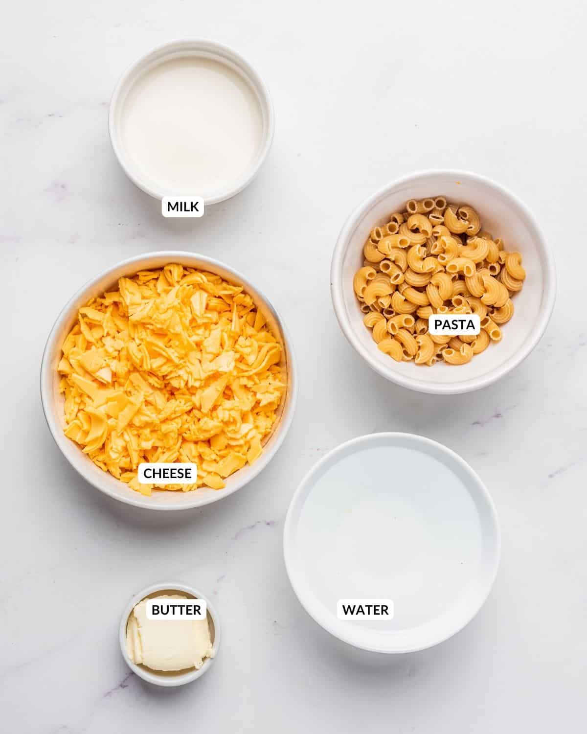 An image of the ingredients of microwave mac and cheese in separate bowls with labels.