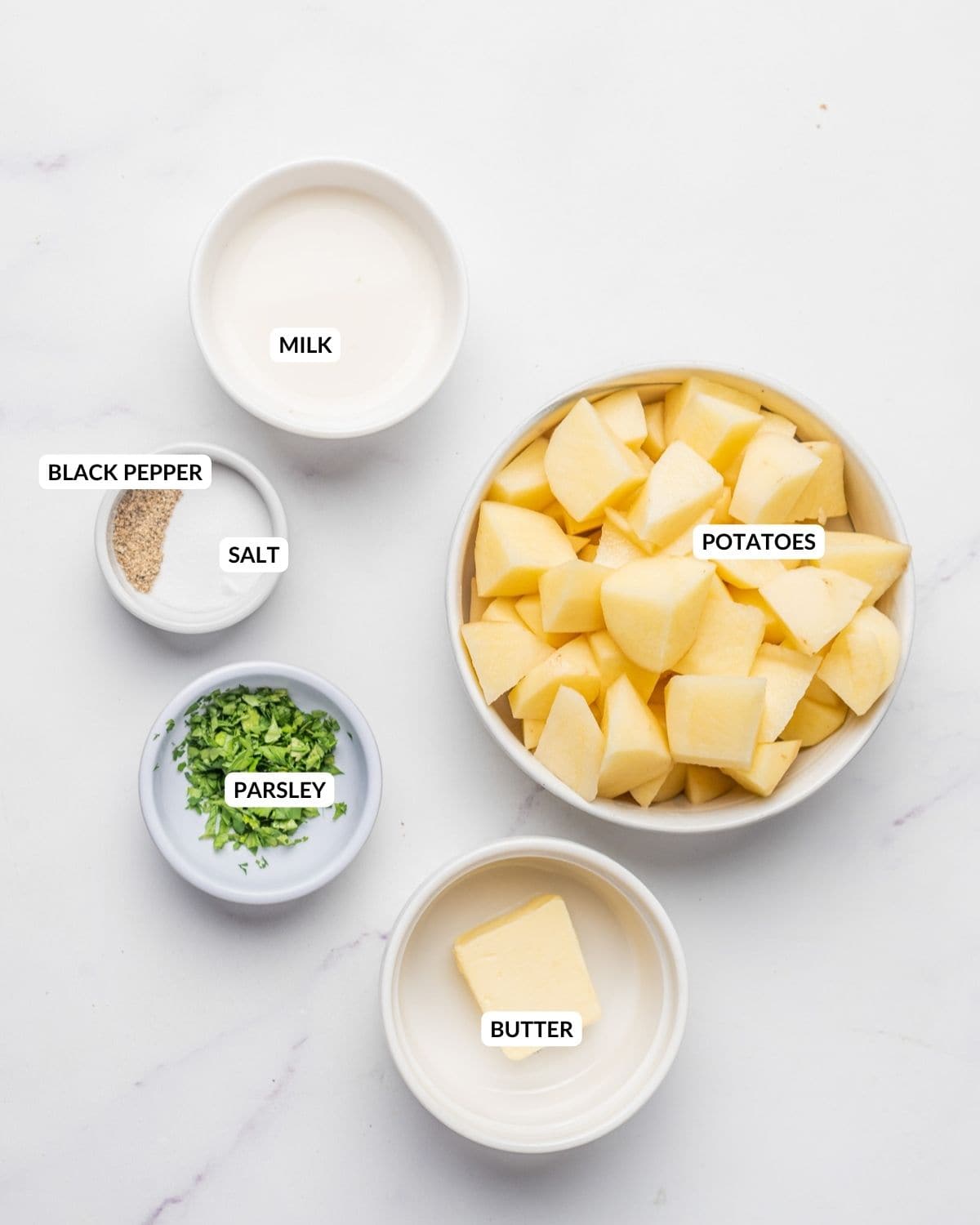 An overhead image of each ingredient of microwave mashed potatoes in separate bowls, with labels.