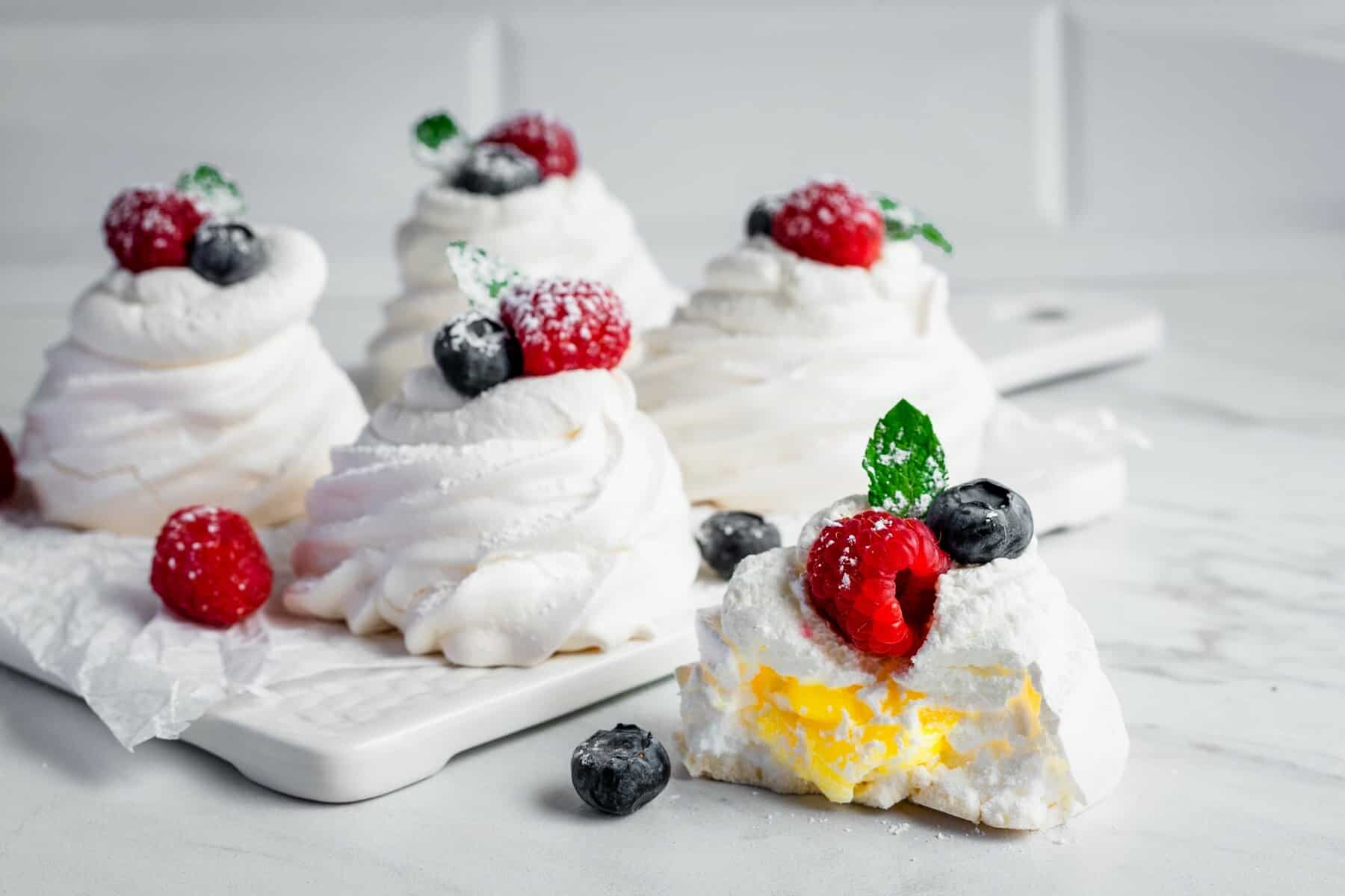A straight view of several mini pavlovas with lemon curd and berries placed on a white platter.