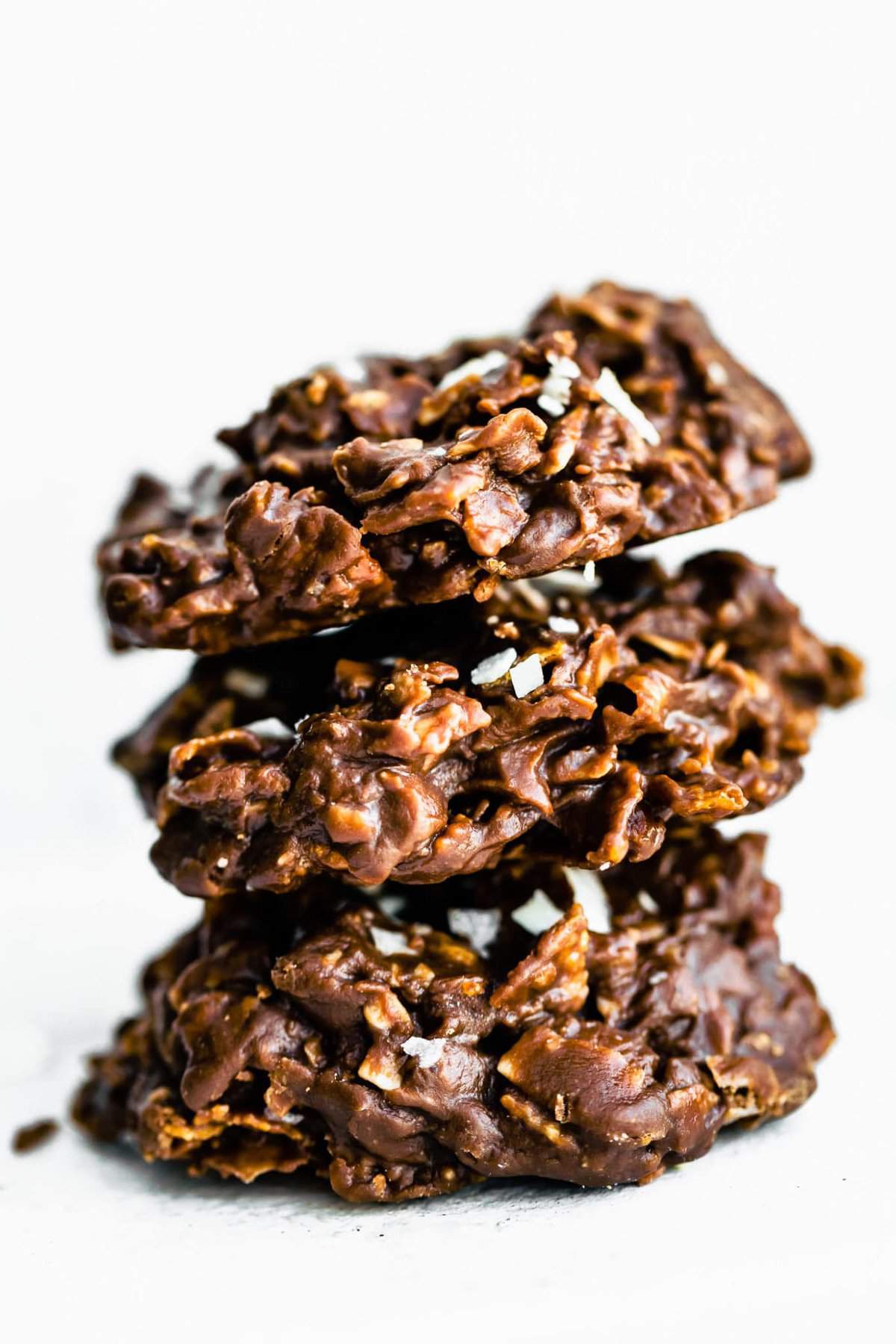 A straight shot of chocolate peanut butter cornflake cookies stacked on top of each other with cornflakes on top.