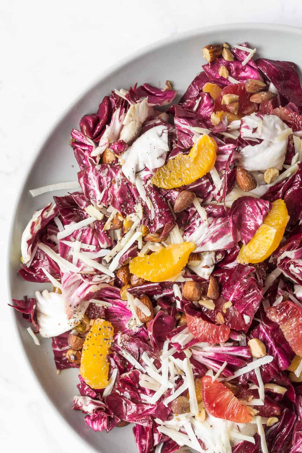 Overhead close-up view of radicchio salad with oranges and pecorino placed on a white plate.