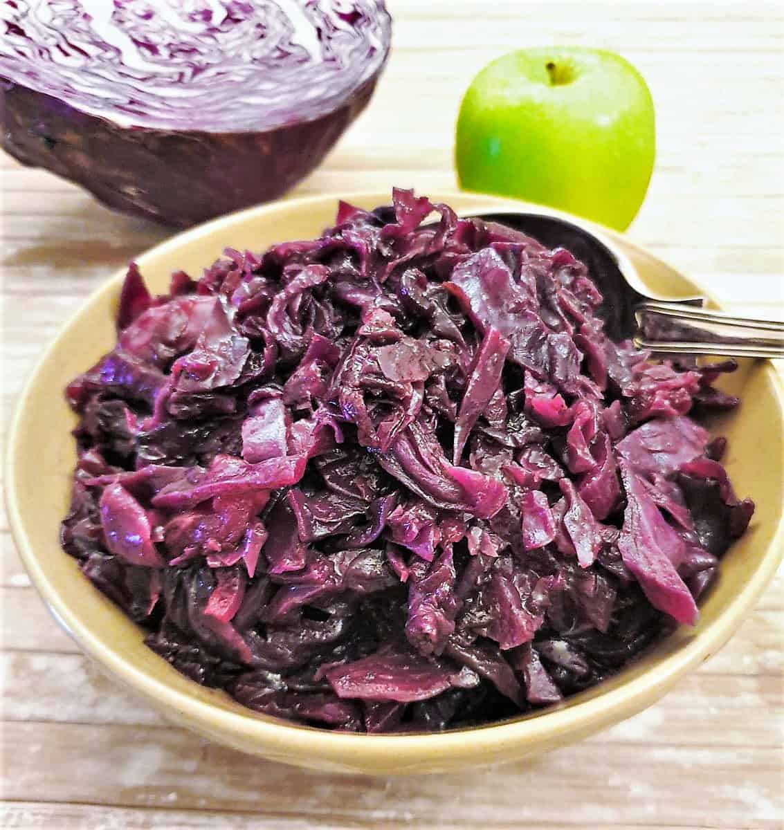 An overhead view of spicy bbraised red cabbage with raw apple and red cabbage in the background.