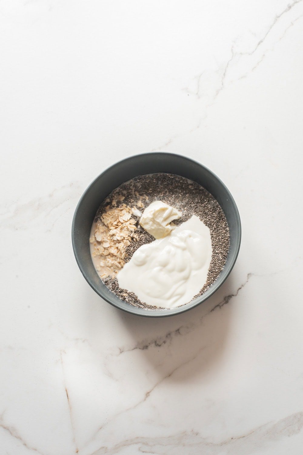 Overnight oats ingredients including oats, chia seeds, cottage cheese, and cream cheese in a bowl before mixing.