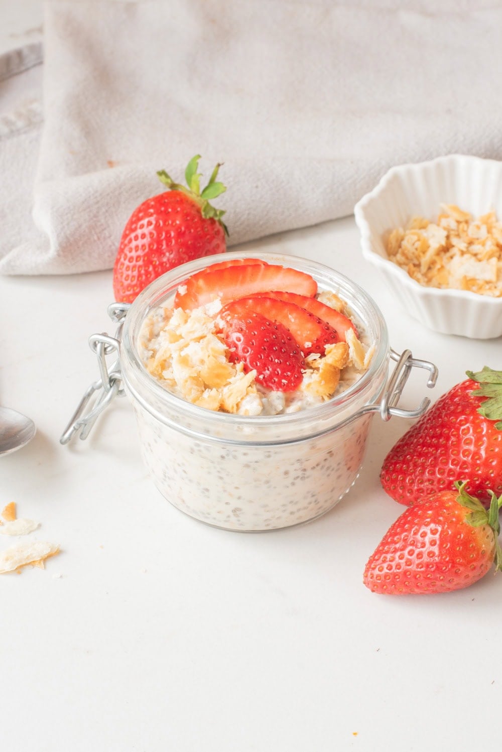 Strawberry cheesecake overnight oats in a glass jar topped with sliced strawberries and graham cracker crumbs.