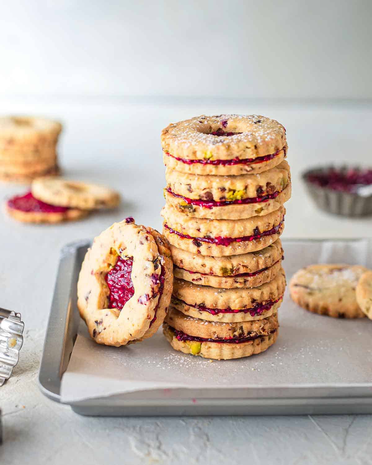 A straight shot of stacked vegan christmas cookies with pistachio and cranberries placed in a baking tray.