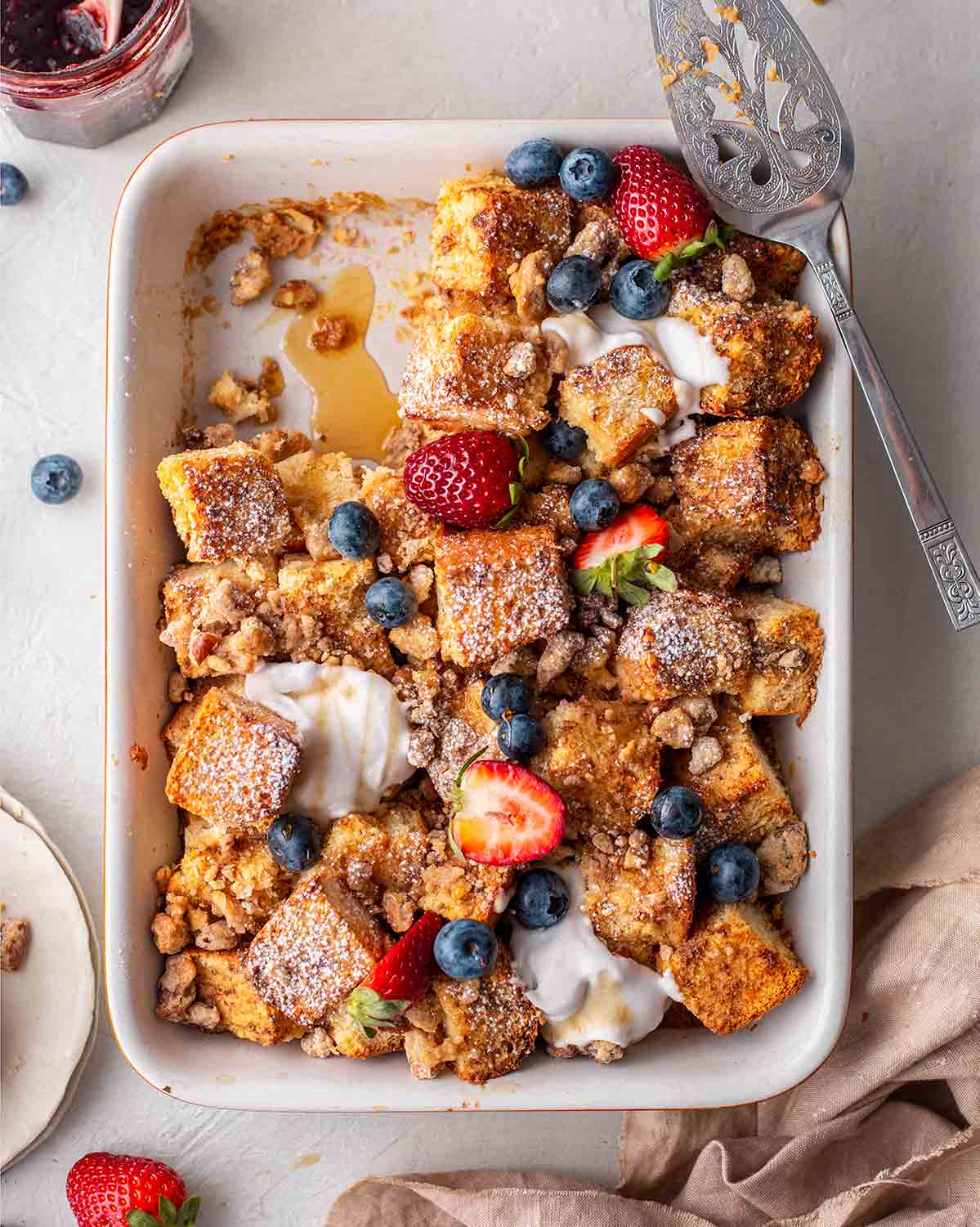 An overhead view of a vegan French toast casserole with berries, pecans, and cream on top.
