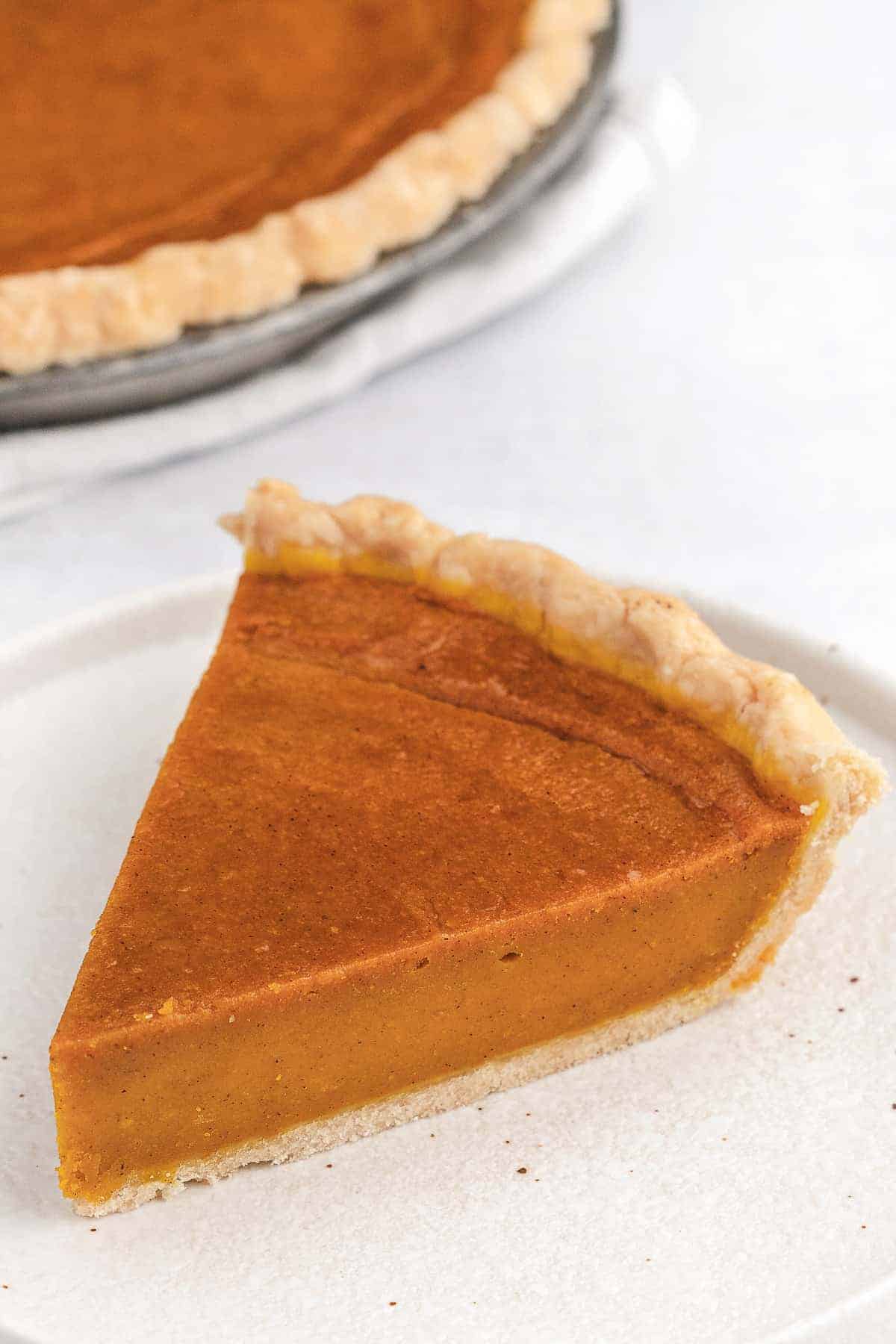 An overhead view of a slice of vegan pumpkin pie placed on a white plate.