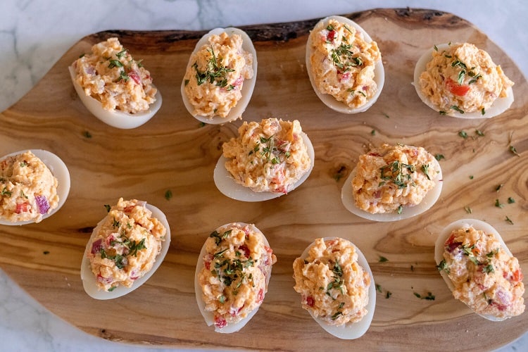 An overhead view of vegan pimento cheese deviled eggs placed on a wooden board. 