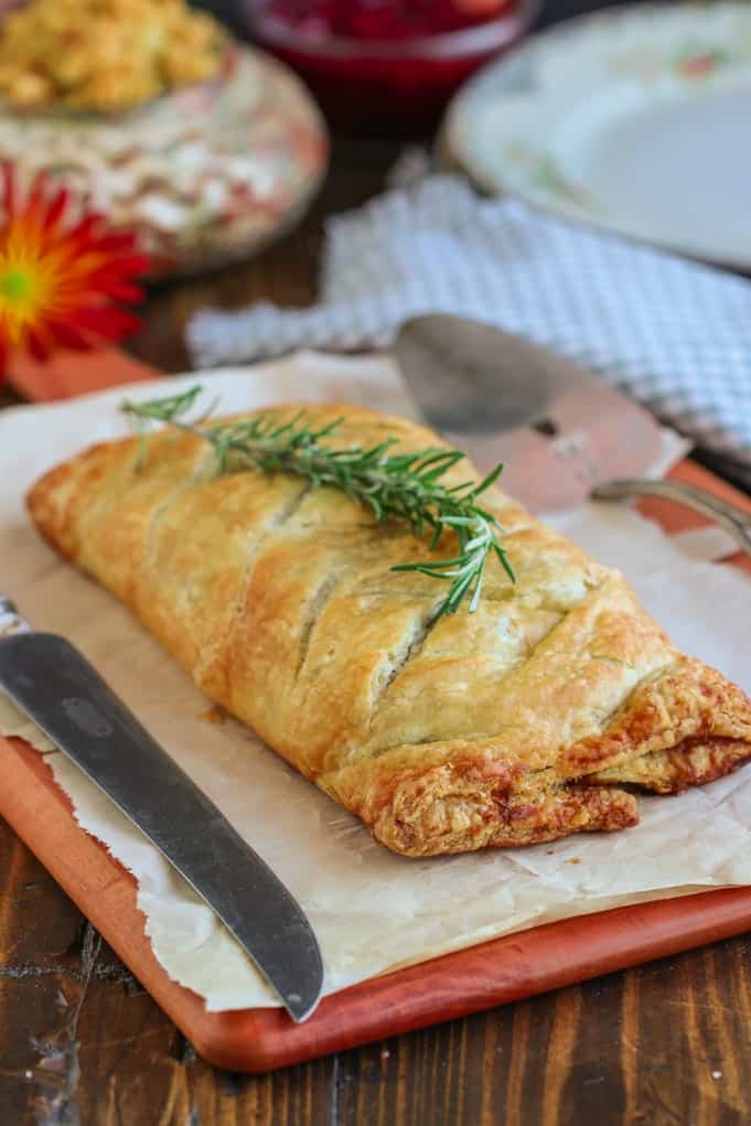 A straight view of the Vegan Mushroom Wellington placed in a wooden cutting board with springs of rosemary on top.